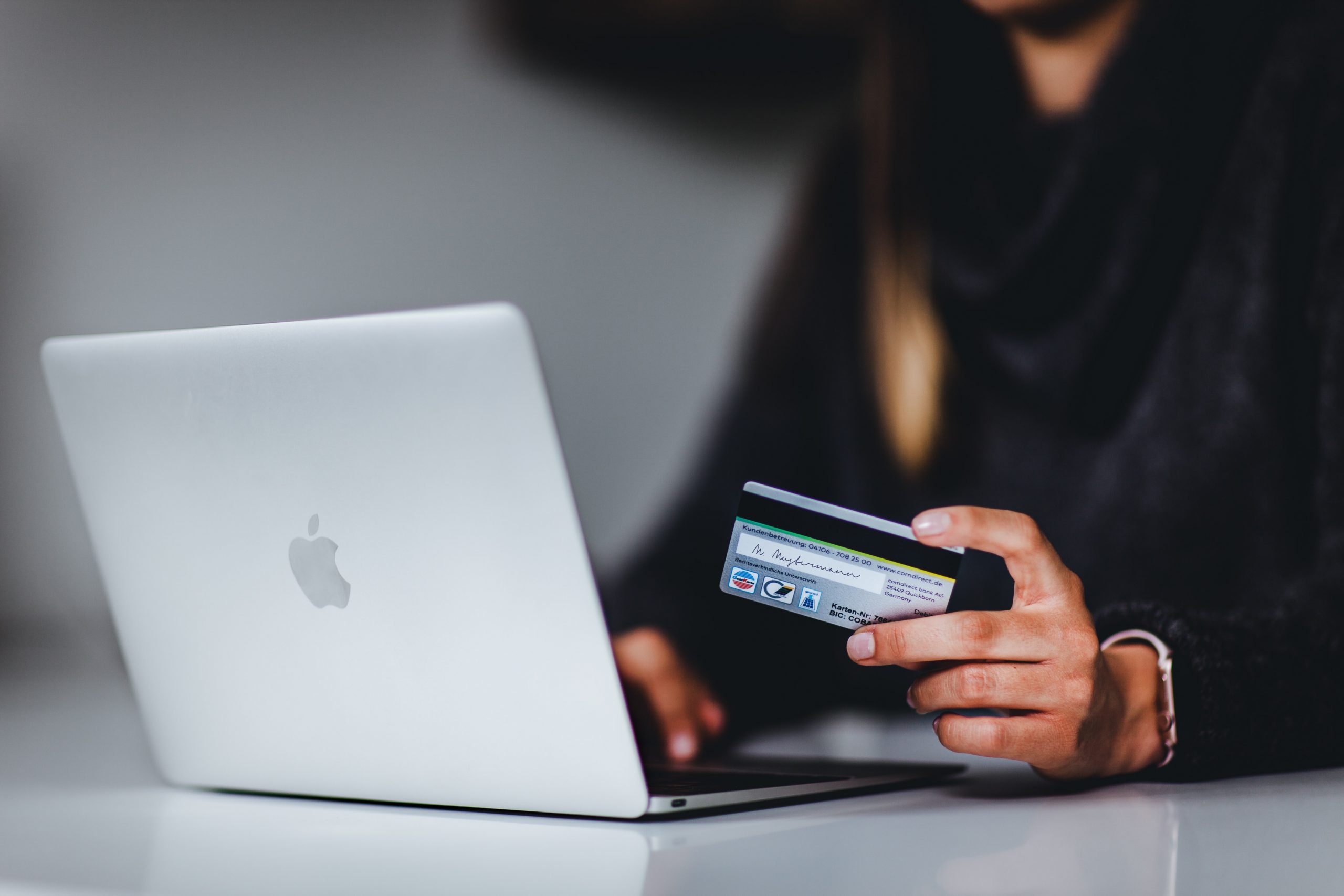 Image shows someone sat at a laptop with their credit card out to illustrate online shopping