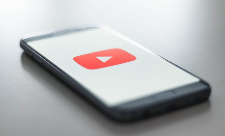 Image shows a mobile phone placed on a table with the youtube video symbol displayed on screen