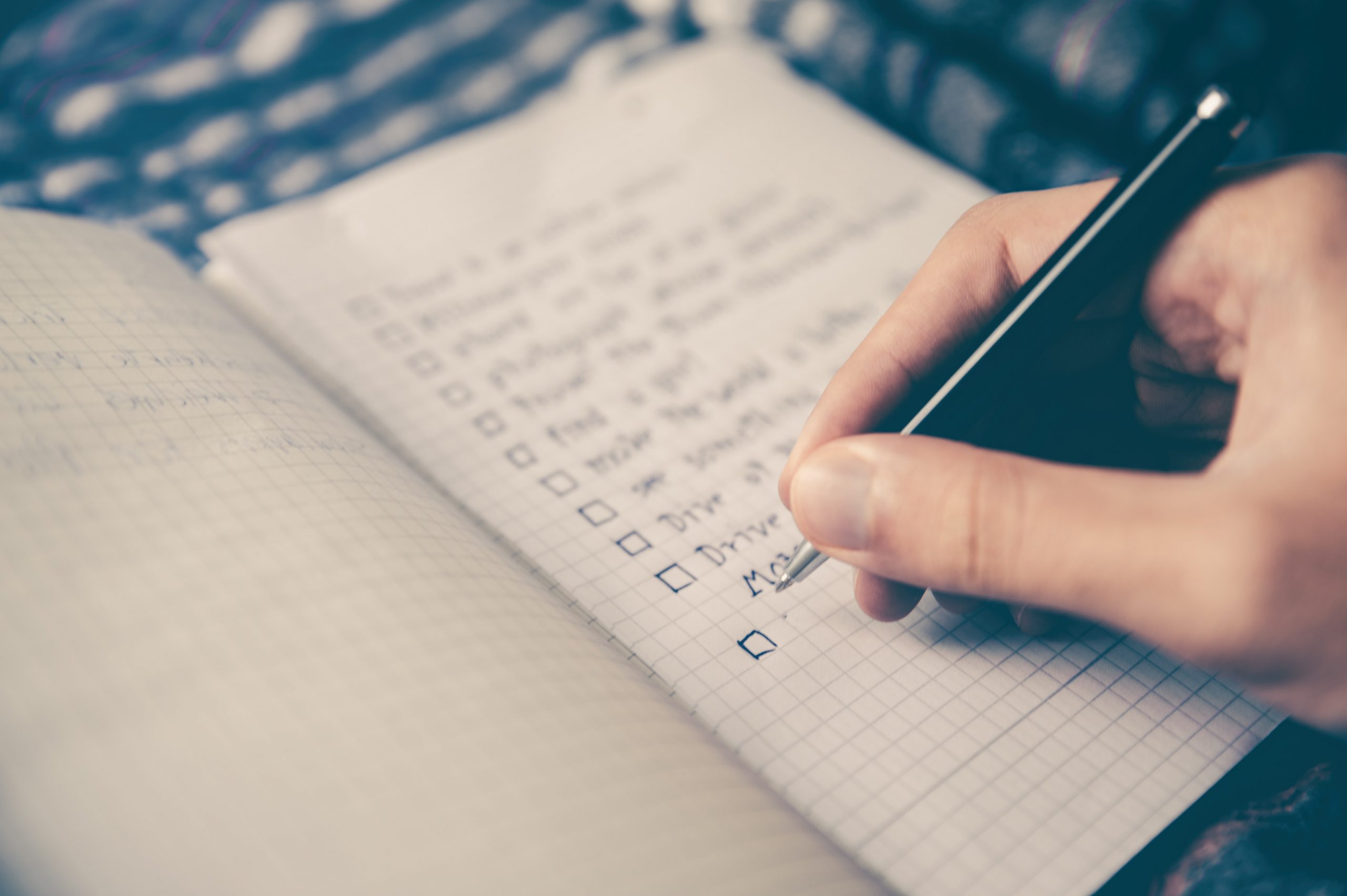 Image is a close up of a hand holding a pen and making a list in a notebook. It is used in the blog post to depict someone planning an instructional video.