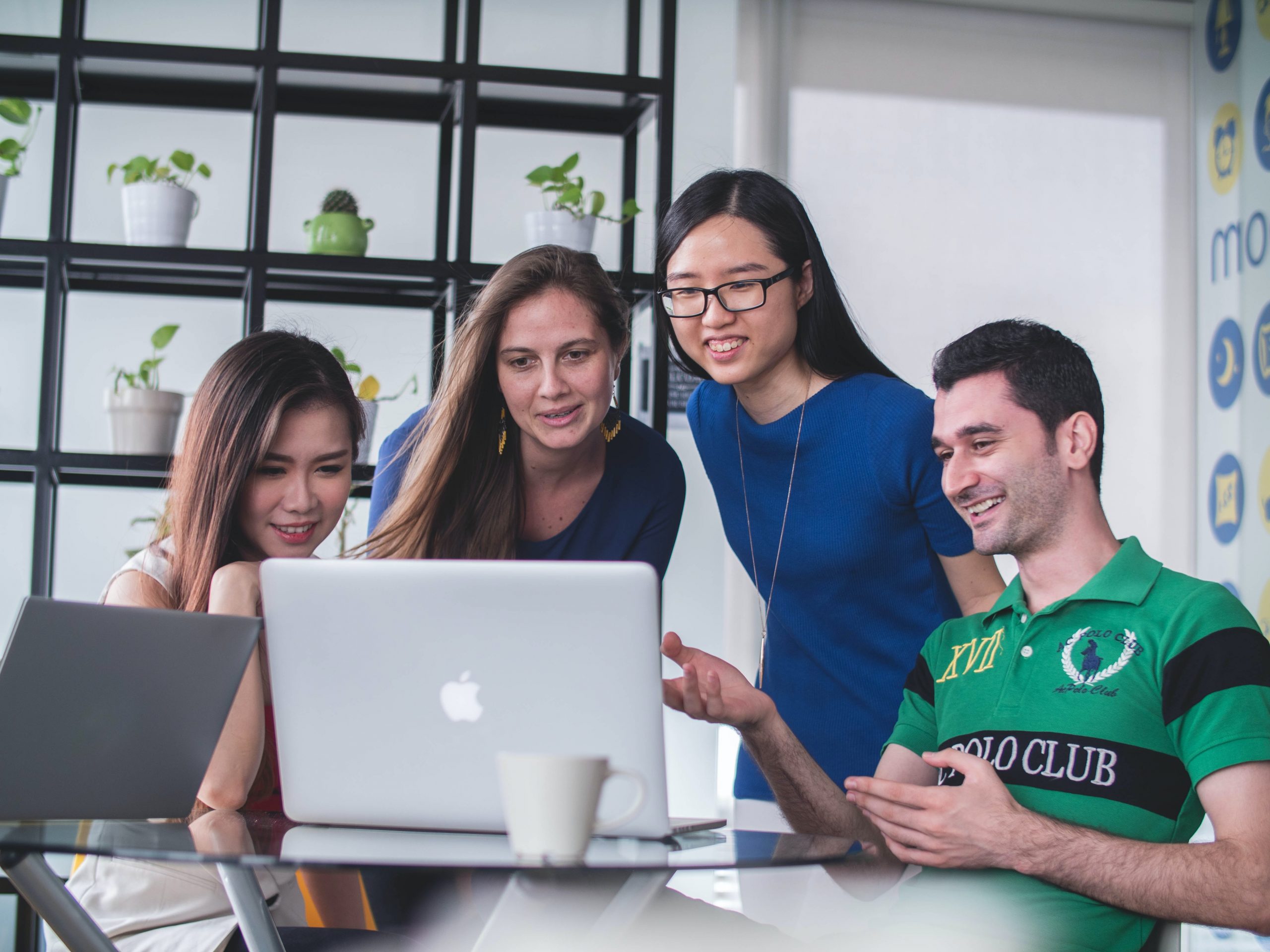 Image shows a group of young professionals gathered around a laptop watching an instructional video for staff training