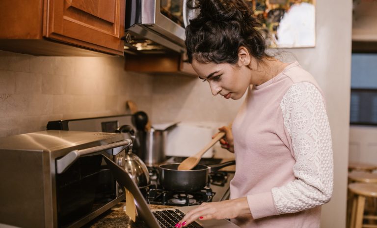 Image shows a woman cooking, using an instructional video to know what to do