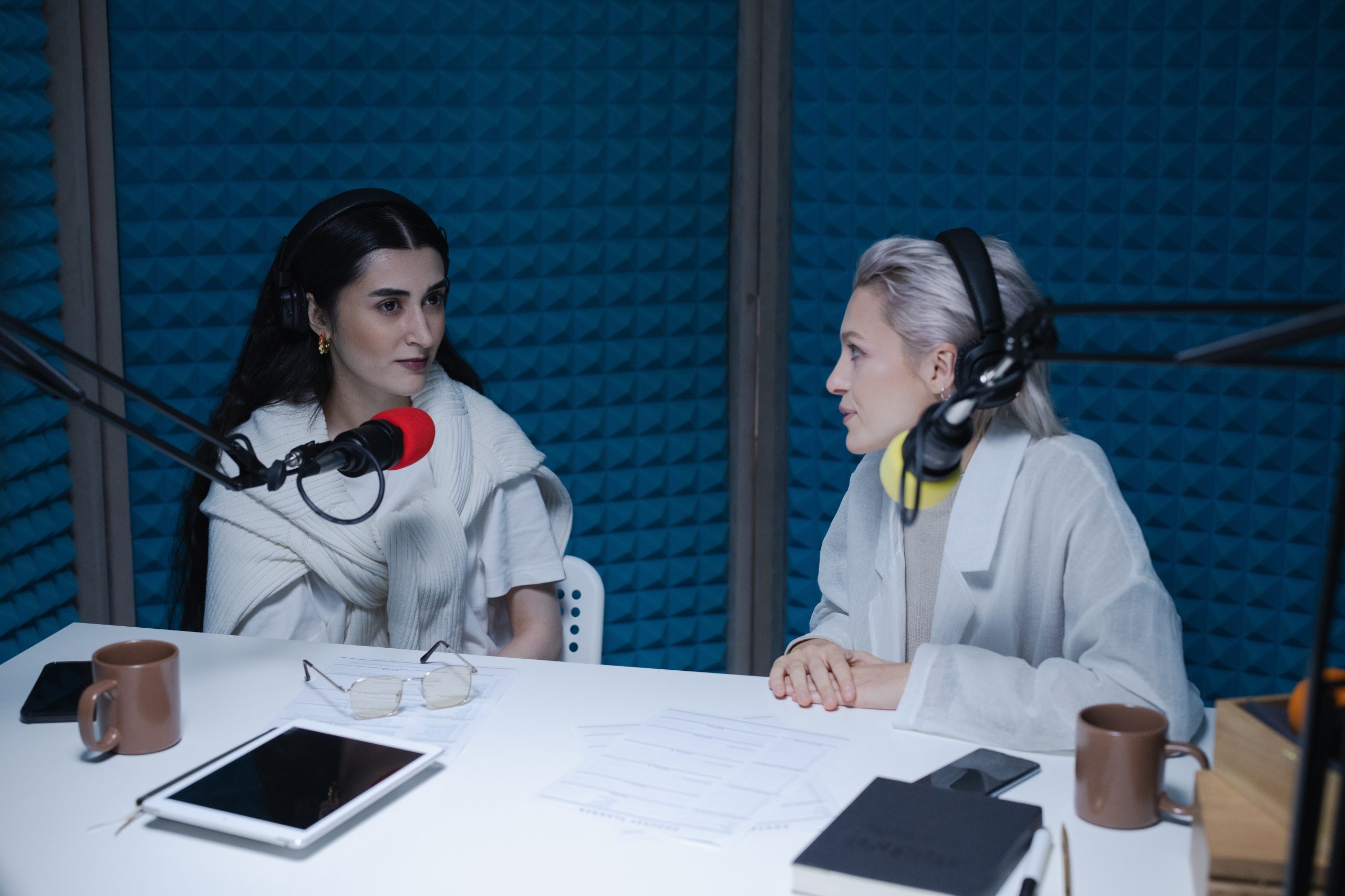 Two women recording a video podcast, in a studio with sound proofing on the walls