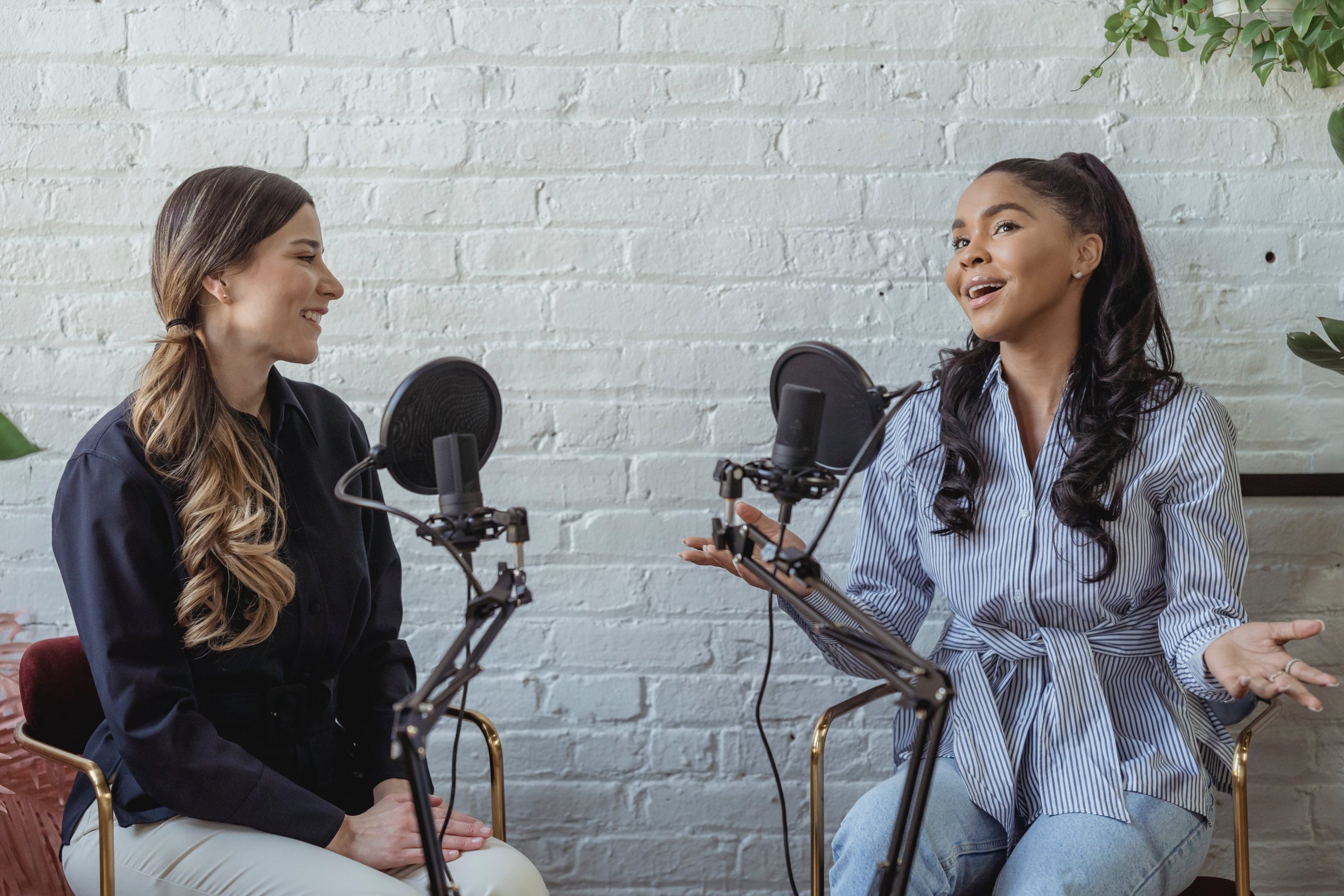 Two women with microphones in front of them, recording a video podcast